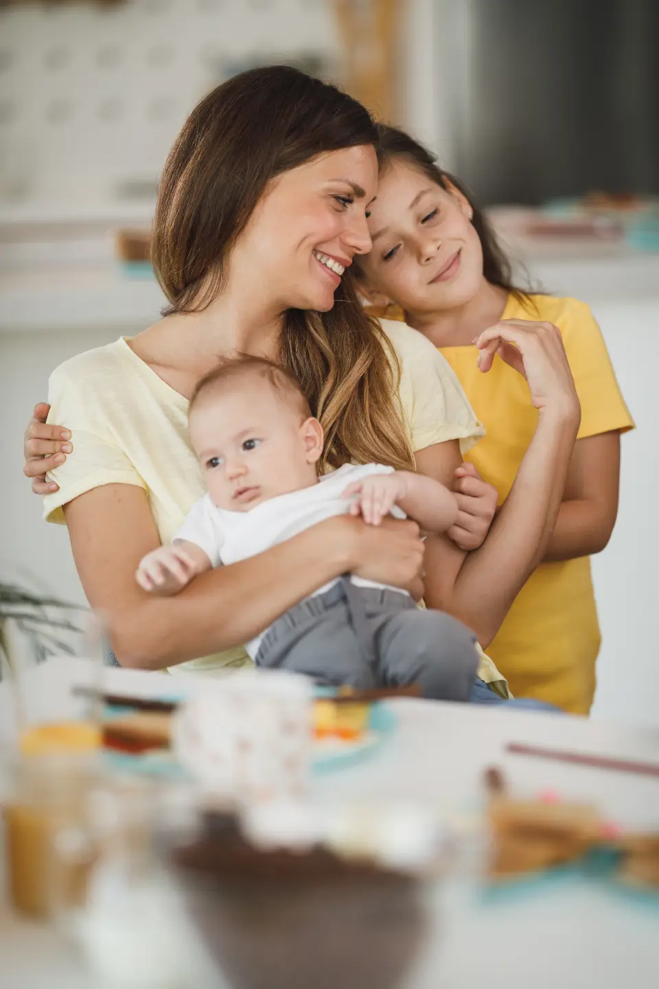 A mother holding her baby, her older daughter leaning against her, all at ease