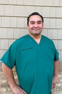 Dr. Martin Ruelas, standing outside the practice in teal scrubs